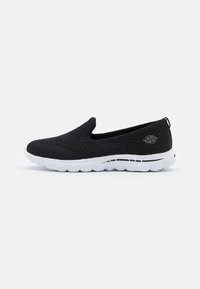 Black slip-on shoes with a textured upper, white rubber sole, and minimal branding detail. Designed for comfort and easy wear.