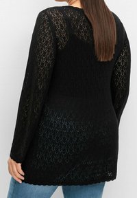 Černý krajkový svetr s dlouhými rukávy, zdobený vzorem diamantů a zakončený vlnitou lemem. Lehká tkanina s texturovaným, otevřeným pleteným designem.