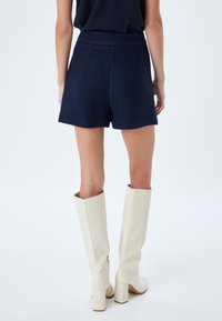 Navy textuur shorts met een hoge taille en zijzakken, gecombineerd met kniehoge witte laarzen met vierkante hakken en een glanzende afwerking.