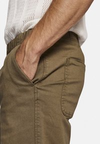 Olijfgroene broek heeft een zijzak en een textuurstof. De tailleband is elastisch voor comfort, met nette stikdetails.