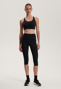Soutien-gorge de sport noir et leggings capri taille haute en tissu extensible. Présente un design épuré sans motifs visibles ni accent matériel.