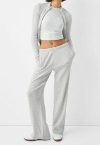 Cardigan grigio a costine con zip, indossato su un top corto grigio chiaro e pantaloni grigi a vestibilità ampia con tasche laterali. Per completare l'outfit, sneakers bianche.