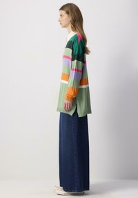 Pull en tricot avec des rayures multicolores vertes, roses, violettes et oranges. Assorti avec un pantalon en denim taille haute, à la coupe décontractée.