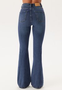 Donkerblauwe high-waisted flared jeans van denim. Beschikt over twee achterzakken en een leren label op de tailleband. Gladde textuur.