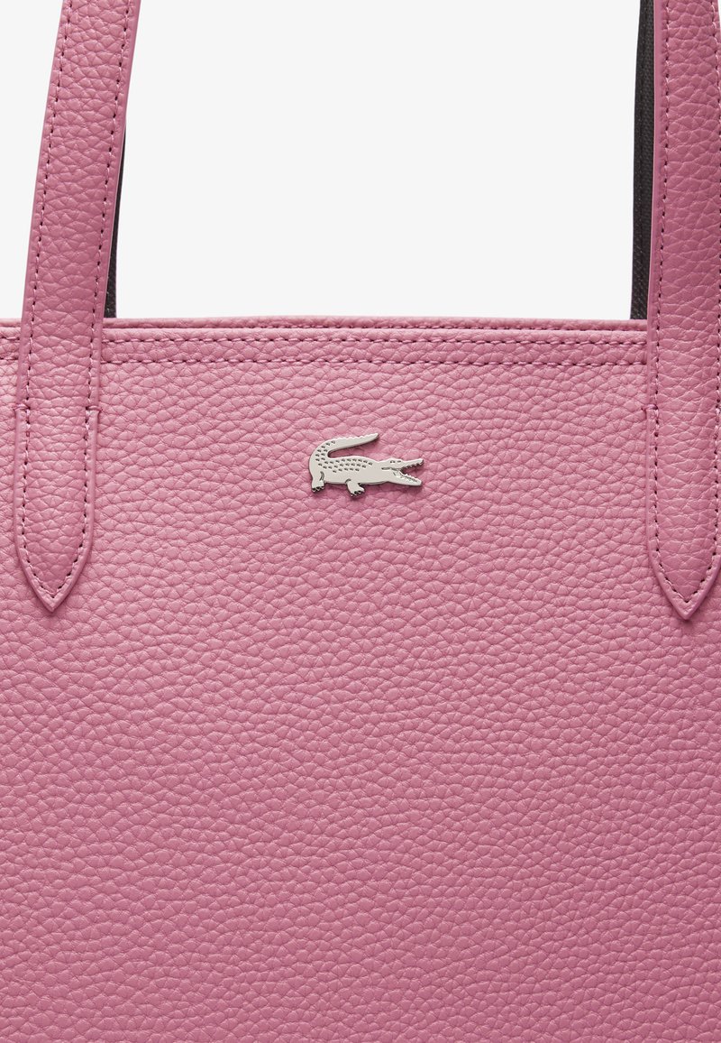 Bolsa tote de cuero rosa con un acabado texturizado, que cuenta con dos asas y un acento de logotipo de cocodrilo plateado en la parte delantera.