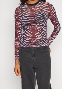 Kvinde iført en tætsiddende langærmet top med pink, sorte og røde tigerstriber og "Juicy Couture"-logo, kombineret med sorte højtaljede jeans.