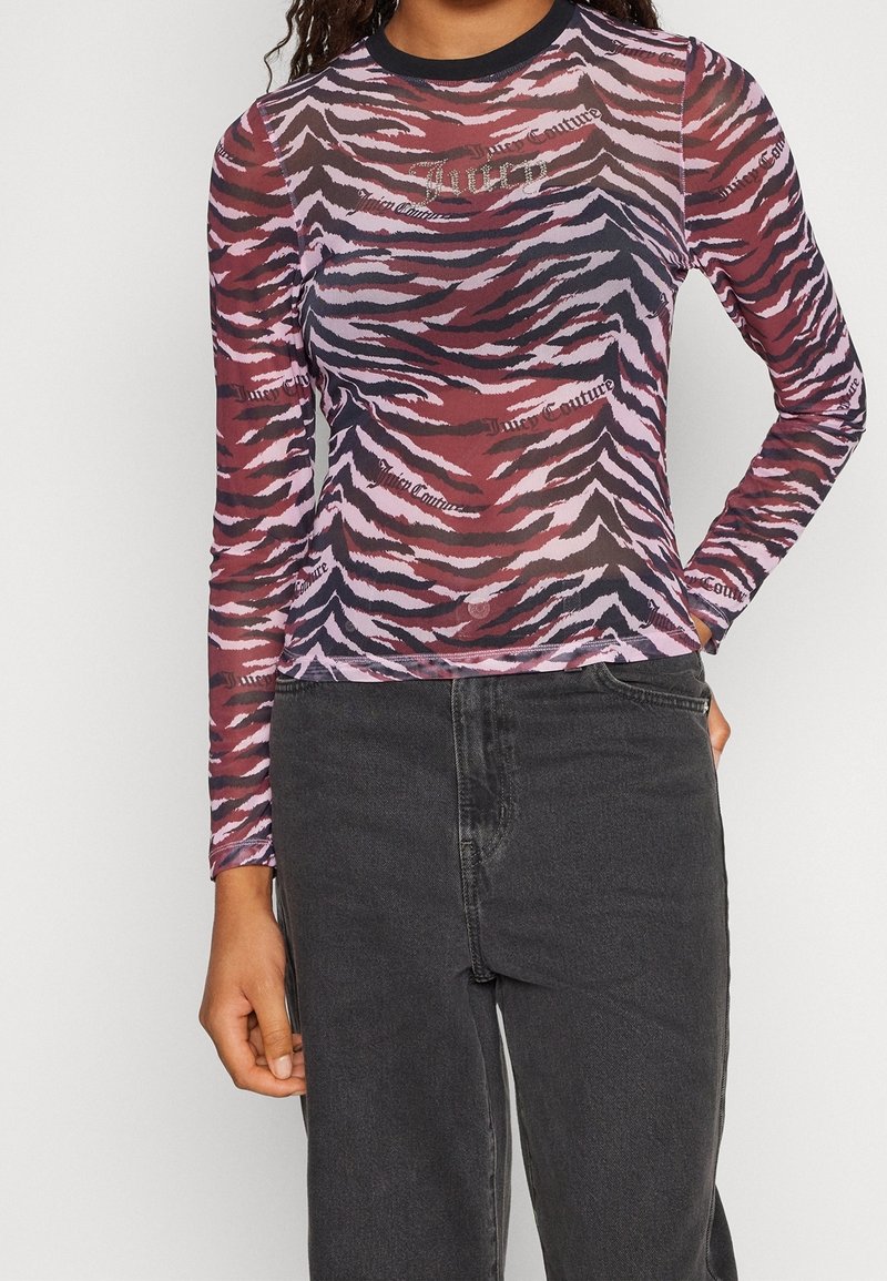 Kvinde iført en tætsiddende langærmet top med pink, sorte og røde tigerstriber og "Juicy Couture"-logo, kombineret med sorte højtaljede jeans.