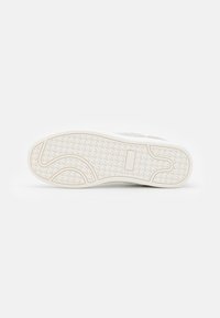 Vitt sneakersula med en texturerad gummiyta och mönstrad grepp, inklusive kurviga mönster och varumärkesdetaljer.