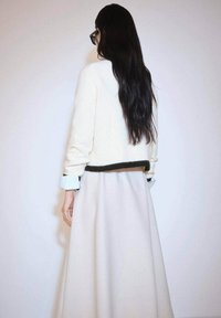 Cream ribbed sweater with dark green trim, paired with a flowy light beige skirt. Long black hair and layered cuffed sleeves visible.