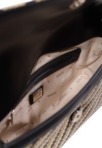 Intérieur de sac à main noir et beige avec doublure en tissu, accents métalliques, poche zippée et motif de logo de marque répétitif.