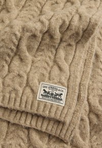 Béžový sveter s pleteným vzorom z mäkkej tkaniny, s textúrovaným vzorom a značkovou nášivkou s retro dizajnom na spodnej časti.