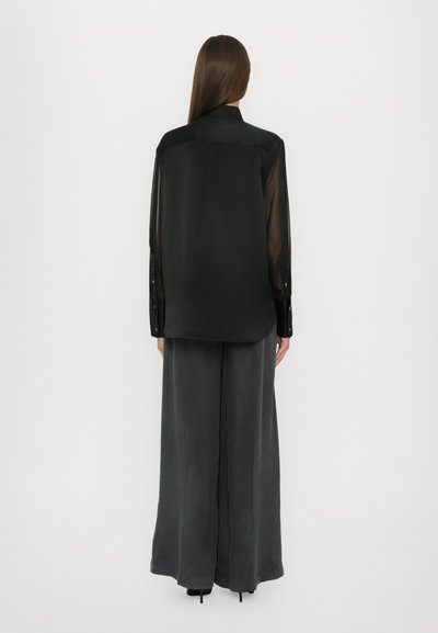 Black sheer long-sleeve shirt with a buttoned collar, paired with loose, dark gray trousers. Simple design, smooth texture, and relaxed fit.