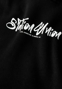 Zwarte stof met een zachte textuur, voorzien van gedurfde witte tekst "Station Union" en "Los Angeles Almeda St." in een gestileerd lettertype.