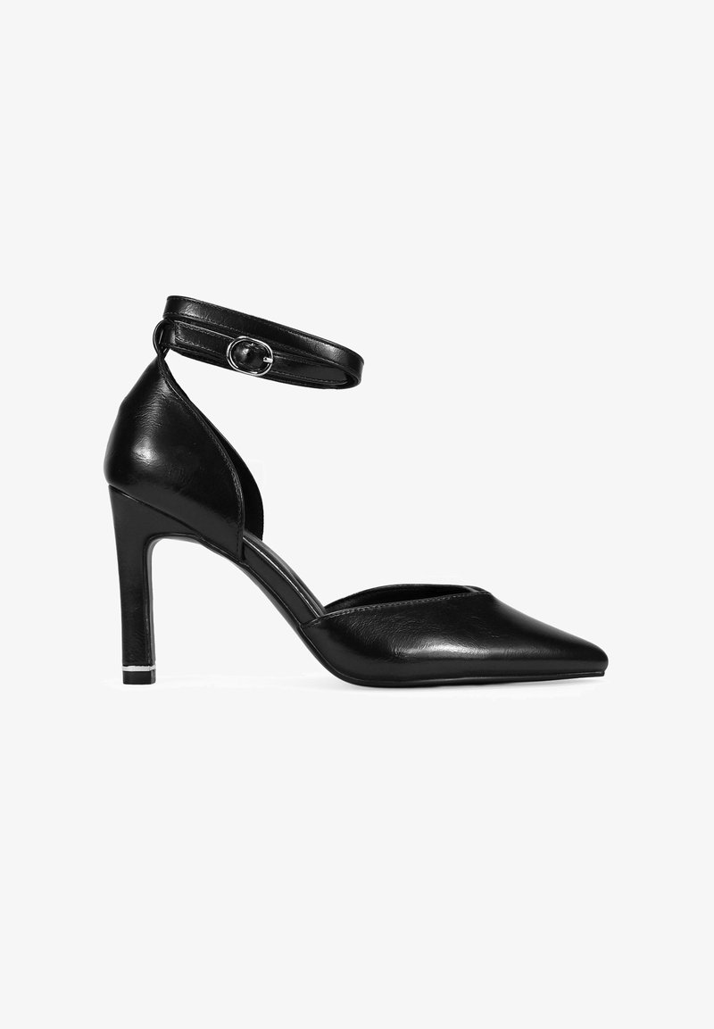 Zapato de tacón alto de cuero negro con punta afilada, correa en el tobillo y un tacón esbelto. Presenta un diseño lateral recortado y un acento plateado en la suela.