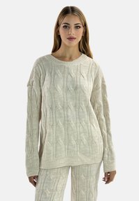 Kremfarvet strikket sweater med kabelmønster, bred halsudskæring og afslappet pasform. Ribstrikkede manchetter og kant tilføjer tekstur til designet.