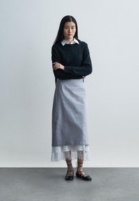 Czarny sweter z dzianiny, szara lniana spódnica z koronkową lamówką, nałożona na białą koronkową podszewkę, zestawiona z czarnymi balerinami na sznurowadła na szarym tle.