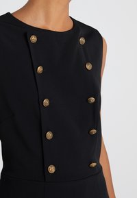 Mustapaitainen ilman hihoja oleva mekko, jossa on pyöreä pääntie ja kuusi kultaa koristenepparia, joissa on kohokuvioidut yksityiskohdat edessä. Sileä kangas.