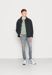 Zwart gestreepte jas, groene t-shirt, licht verwassen jeans en meerkleurige sneakers. Gecombineerde outfit met verschillende texturen en kleuren.
