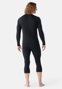 Zwarte lange mouwen compressie shirt en driekwart lengte leggings, met een gladde textuur en een aansluitend ontwerp. Geen zichtbare merknamen.