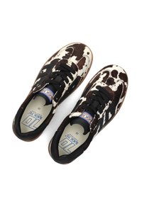 Sneakers in pelle di vitello bianca e marrone con lacci neri, con un profilo basso, una parte superiore testurizzata e un'etichetta blu e bianca all'interno.