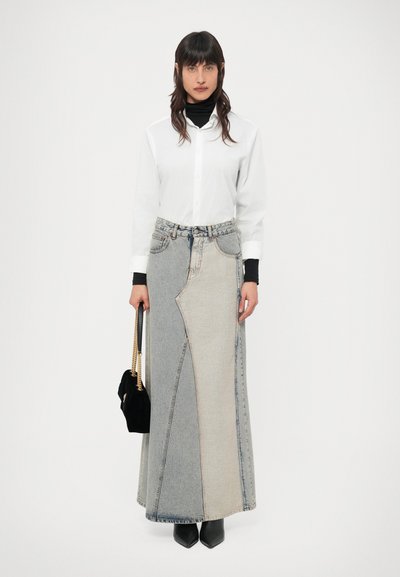 Saia maxi em ganga com um padrão em patchwork em tons de azul claro e escuro, combinada com uma camisa branca de botões e botas pretas.