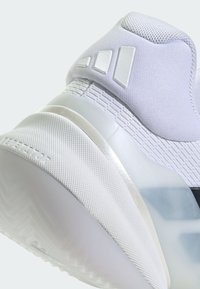 Biela športová obuv s textúrovaným zvrškom, hladkou gumovou podrážkou a kovovými detailmi na päte, ktoré zdôrazňujú moderný, aerodynamický dizajn.