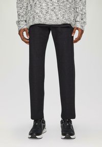 Dunkelgraue, schmal geschnittene Anzughose aus einem strukturierten Stoff. Kombiniert mit schwarzen Sportschuhen, um einen lässigen Look zu betonen.