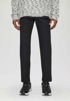 Ciemnoszare spodnie wykroju z slim fit, wykonane z teksturowanej tkaniny. Zestawione z czarnymi butami sportowymi, podkreślając swobodny wygląd.