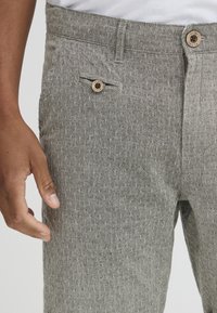 Gray patterned trousers featuring a textured fabric, a button closure, and a front pocket with a decorative button detail.