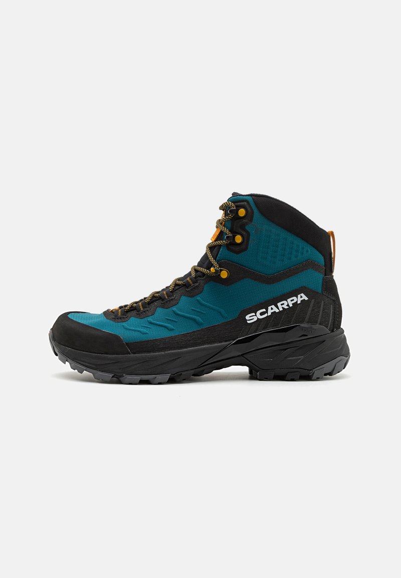Botte de randonnée mi-haute avec une tige teal et des accents noirs, un embout en caoutchouc, des accessoires dorés et un détail texturé sur le côté.