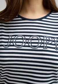 T-shirt a righe blu navy e bianche con scollo rotondo, caratterizzato da ricamo del testo 'JOOP!' in blu e bianco. Tessuto morbido con una vestibilità casual.