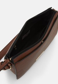 Brązowa skórzana torba crossbody z zamkiem błyskawicznym, wewnętrzną czarną podszewką i złotym akcentem wykończenia. Kompaktowy prostokątny kształt.