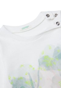 Bílé bavlněné tričko s kulatým výstřihem a patentkami. Má pastelový květinový potisk se zelenými akcenty a značkovou etiketu.