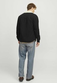 Zwarte shirtjasje met een zachte witte fleece kraag, knoopsluiting en lange mouwen, gecombineerd met lichtblauwe baggy jeans.