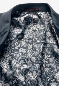 Interiér blejzru s námořnickou květinovou podšívkou. Obsahuje světle modré a bílé květy na tmavém pozadí, hladkou texturu a klasický design.