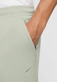 Light green Nike sweatpants feature a smooth texture, elastic waistband, side pocket, and a subtle logo on the left thigh.