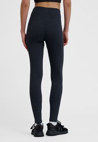 Mörkgrå leggings med en slät, elastisk textur och en hög midja. Bärs med svarta sportskor och vita strumpor.