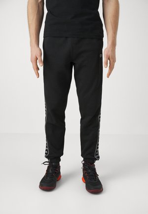 Black sweatpants with a slim fit, featuring white side stripes and an elastic waistband, paired with black athletic shoes.
