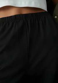 Černé elastické kalhoty s elastickým pasem, s hladkou texturou a minimálními švy. Design je jednoduchý a univerzální.