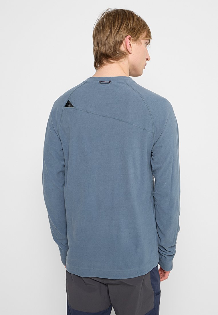 Chemise bleu à manches longues en tissu doux, présentant une couture diagonale dans le dos et un petit accent triangulaire noir.