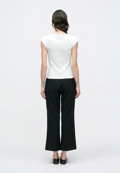 Λευκό ριμπ κοντομάνικο τοπ συνδυασμένο με μαύρο παντελόνι φαρδιάς γραμμής. Το τοπ έχει εφαρμοστή σχεδίαση, ενώ το παντελόνι έχει λεία υφή.