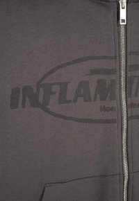 Szary hoodie na zamek wykonany z miękkiego materiału, z dużym czarnym nadrukowanym logo "INFLAM" w owalnym obrysie oraz z kieszeniami z przodu.