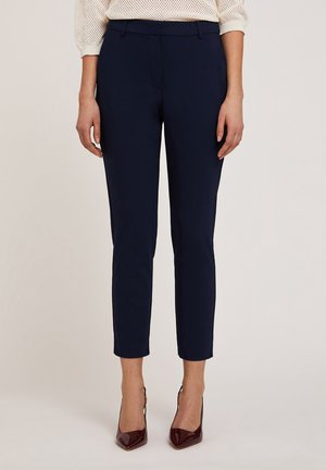 Pantaloni blu navy su misura con vestibilità slim, caratterizzati da una texture liscia, vita media e dettagli piegati. Abbinati a tacchi bordeaux lucidi.