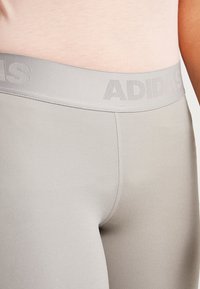 Vaaleanharmaat legginssit, joissa on teksturoitu vyötärö ja "ADIDAS" hieman tummemmalla harmaalla. Sujuva kangas, tiukka malli, minimaaliset saumat.
