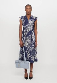 Rochie de marină cu imprimeu alb de frunză de palmier, mâneci scurte, talie obișnuită și fustă fluidă. Geantă de mână bleu deschis cu detalii de curea și cataramă.