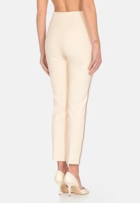 Pantaloni aderenti di colore crema con un design elegante, caratterizzati da una striscia laterale, una texture liscia e una vita a media altezza.