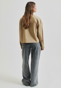 Cămașă oversized khaki din bumbac, cu mâneci lungi și mansete cu nasturi, asociată cu blugi gri din denim cu talie înaltă.