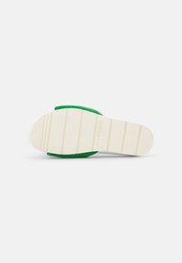 Sandale en daim vert avec une semelle en caoutchouc blanc, présentant une texture antidérapante et des rainures horizontales pour une meilleure adhérence.