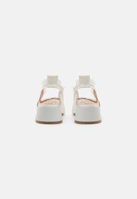 Sandales blanches à dos ouvert avec une finition texturée, sangle ajustable et un talon chunky blanc et brun. Elles présentent une doublure intérieure douce.
