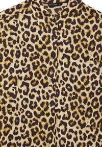 Chemise à boutons avec motif léopard marron, noir et beige et col pointu.
